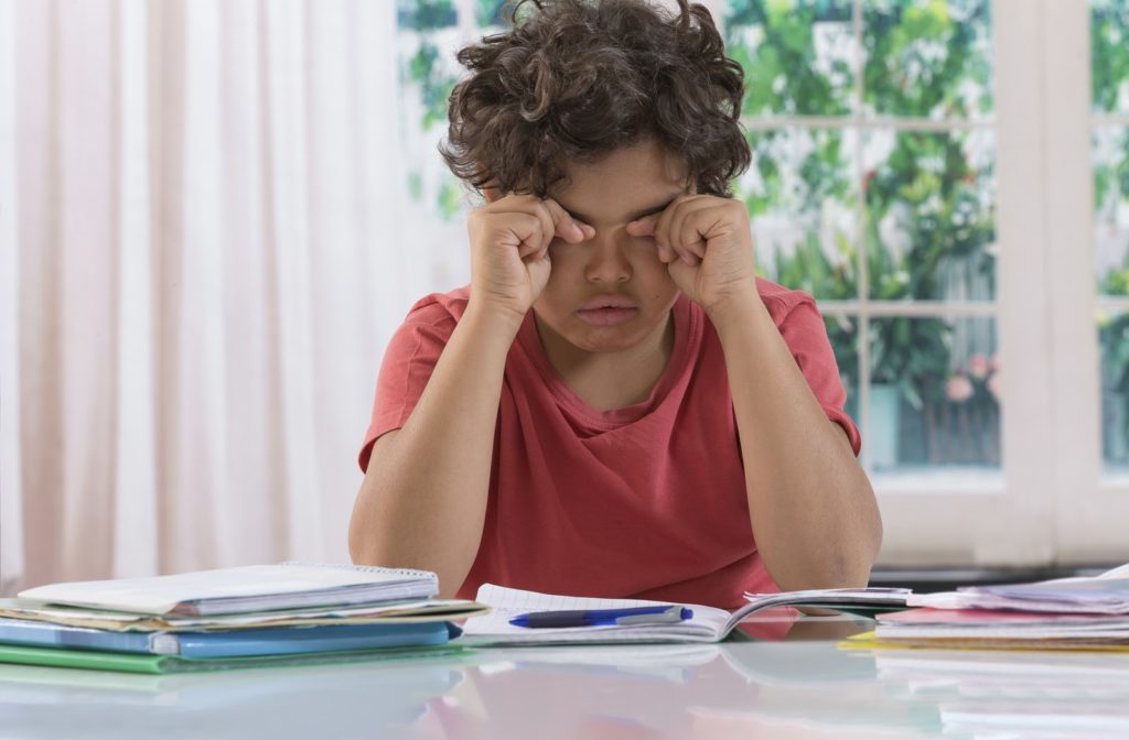 Frustrated boy rubbing his eyes after working on his homework.